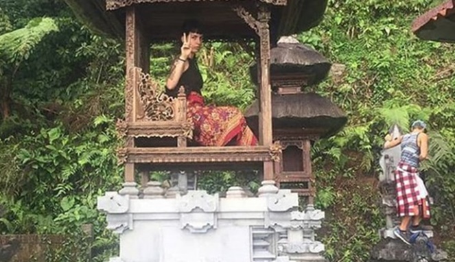 Turis asing duduk di atas pelinggih, tempat suci orang Hindu di Bali. [Sumber Gambar]